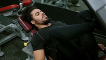 Young man using leg press machine in gym.