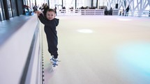 A little boy learns to skate for the first time in an indoor ice rink.