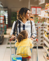 Young Mother and daughter in the cart shopping for groceries in supermarket.