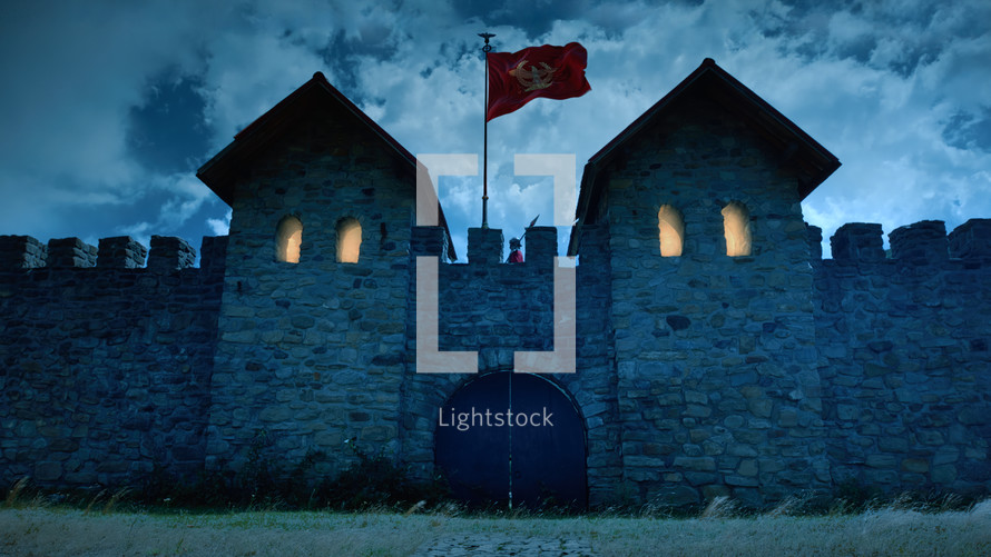 Roman military fort with illuminated windows and the flag fluttering at night.
