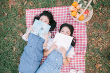girls lying on a picnic blanket reading books 