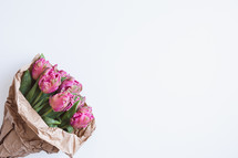 Bouquet of pink tulips in brown paper wrapping on a white background