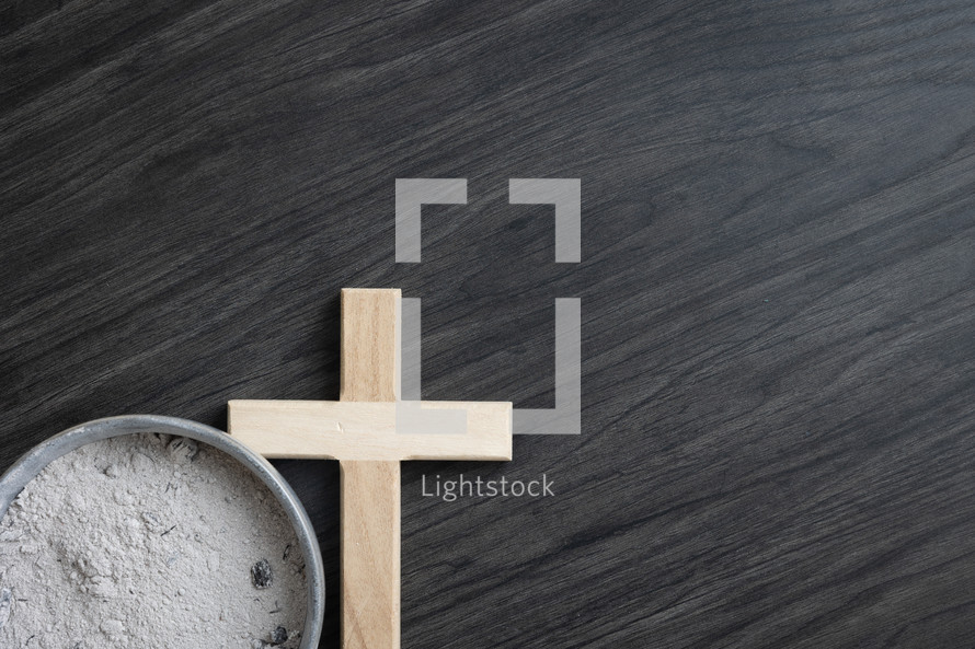 Small wood cross and bowl of ashes on dark wood