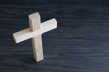 Small wood cross standing on a dark wood table from above