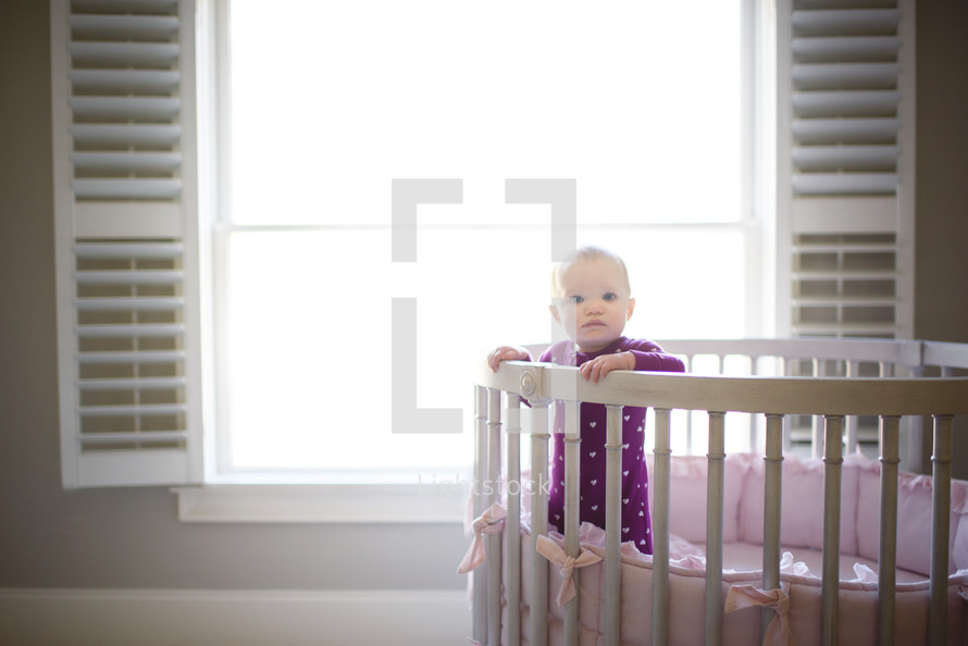 an infant standing in a crib in a nursery 