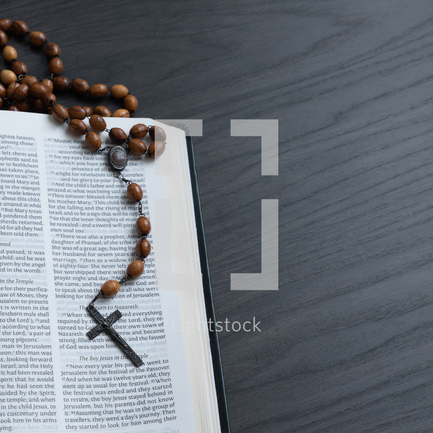 Wood rosary on an open bible on a dark wood background with copy space