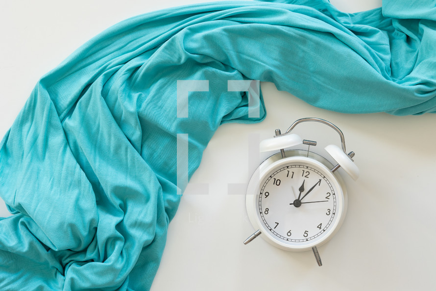 White alarm clock on a white background with a teal blanket
