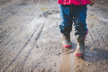 a girl in rain boots walking through a muddy puddle 