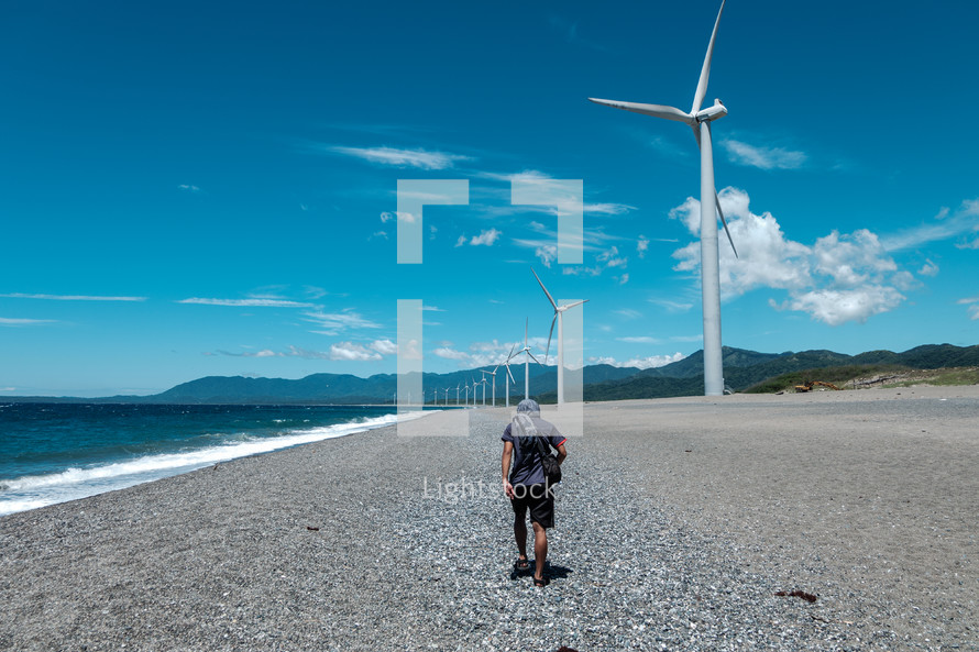 wind turbines along a shore and man walking on beach 