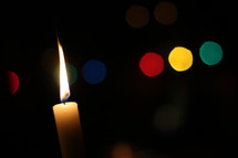 flame on a candle and colorful bokeh lights 