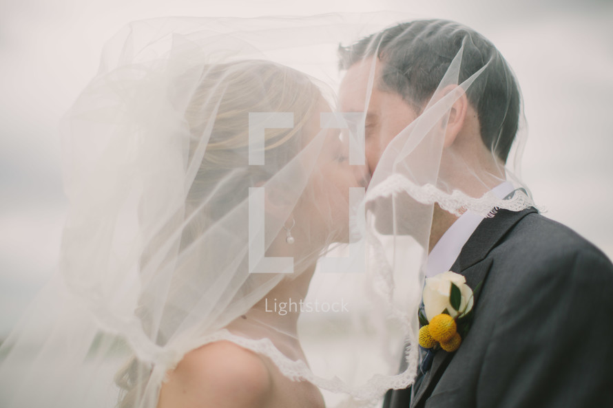 Bride and groom kissing with veil