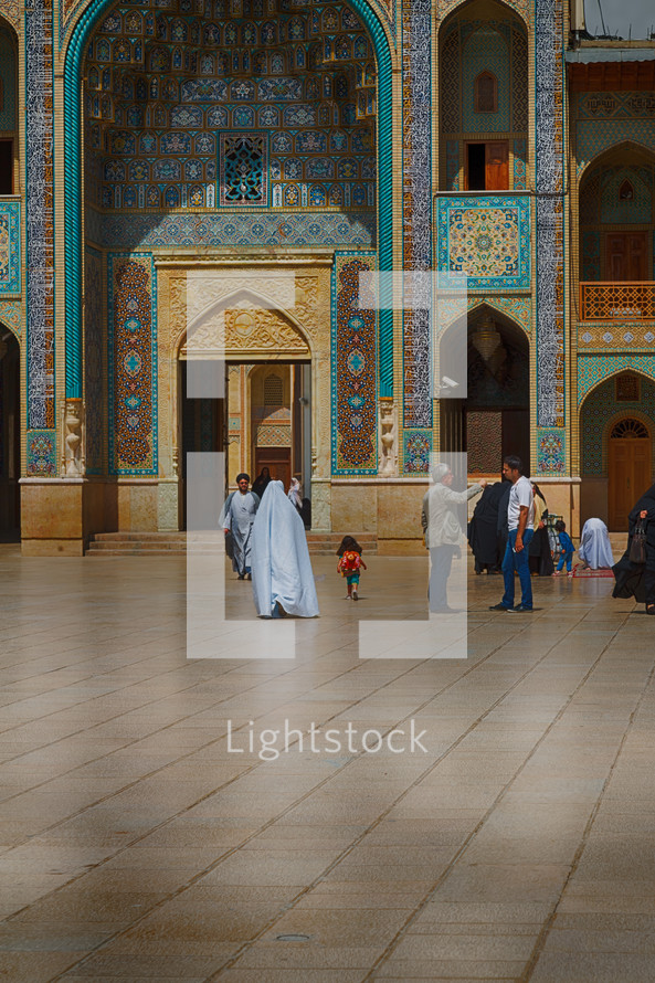 people walking through a courtyard in front of a mosque 