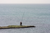 Fisherman sits on a finger of land and fishes in the sea.