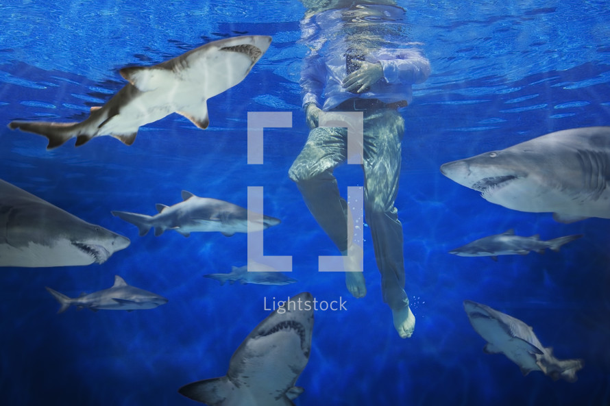 Businessman underwater, surrounded by circling sharks

