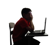 sad child sitting at a desk looking at a computer 