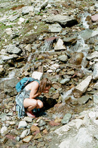 a woman drinking fresh water from a mountain spring 