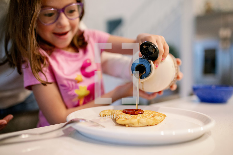 Little girl pouring syrup on her pancakes 
