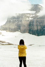 woman taking a picture of snow on a mountaintop 
