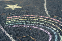 Chalk drawings of a rainbow and star on a concrete driveway.