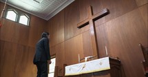 Man kneeling to pray by wooden cross. Young man praying, confessing sin, worshipping  in church in cinematic slow motion.