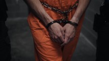 Angry, depressed, hopeless and unhappy man in orange prison uniform and handcuffed, prisoner and criminal being led by prison guards to his cell in cinematic slow motion.