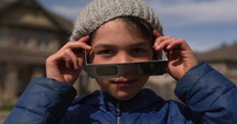 Young boy looks towards camera and puts on solar eclipse glasses to look at sun