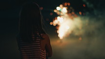 girl watching fireworks on the ground at night 