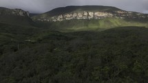 Drone flies over dirt road toward base of mountain covered by clouds