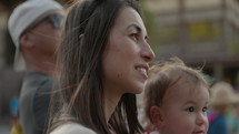 Mother holding toddler watching parade event outdoors - close up on face