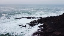 Orbiting drone shot around ocean rocks on an overcast day in Oregon.