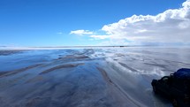 Aerial shot drone flies up and follows jeep through salt flats on cloudy day