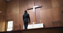 Young man in church looking at a large wooden cross in prayerful, meditative contemplation.