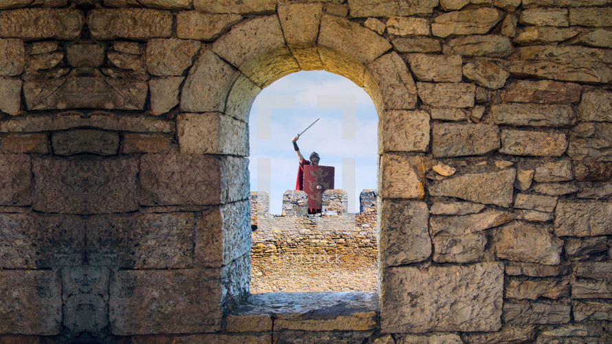 Roman guard raising sword declares victory behind a citadel window.
