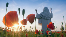 Christ praying with raised hands in a beautiful poppy field at sunset.
