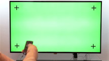Woman hand with TV remote switching channels on a green screen TV