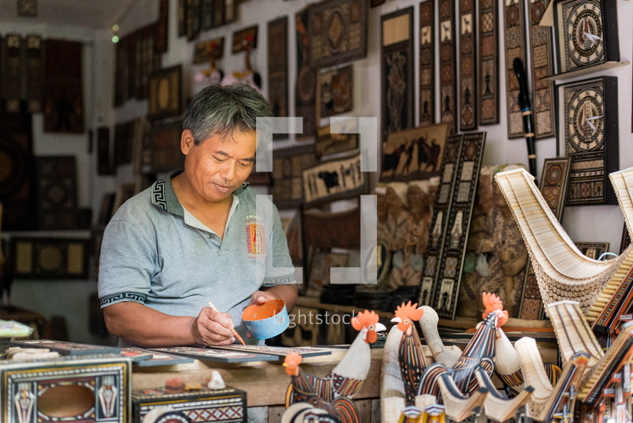 a man carving ornate detail into wood and painting it