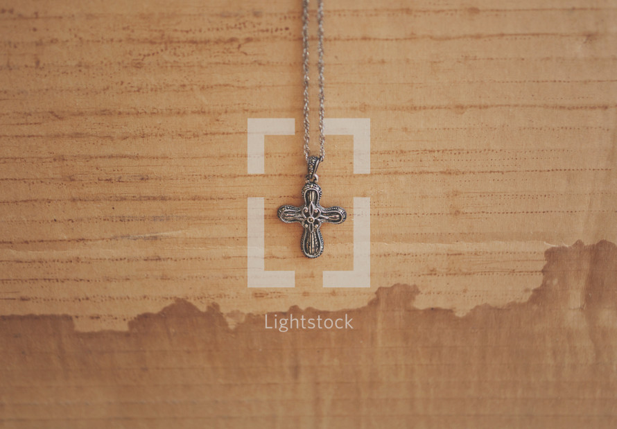 Cross necklace hanging against a stained cardboard background