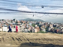 women walking on a dirt road through a poor city 