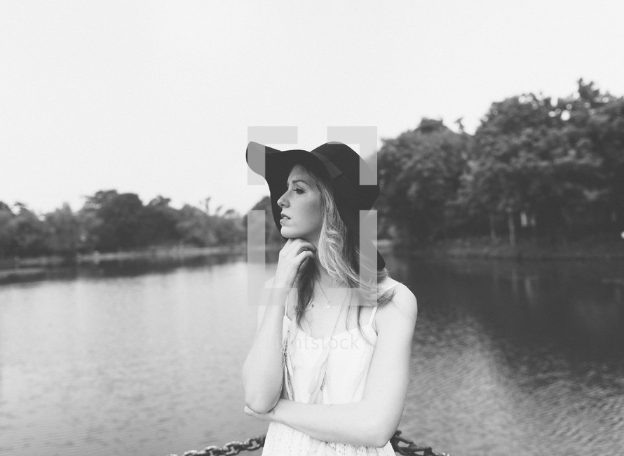 a woman in a sunhat standing by a lake 