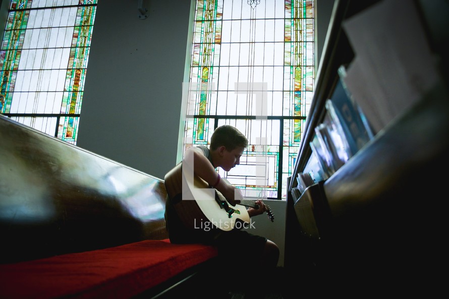 a child playing a guitar sitting in church pews 