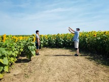 a man taking a picture of a couple standing near a field of sunflowers 