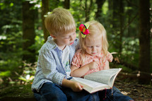 brother and sister reading a Bible together outdoors