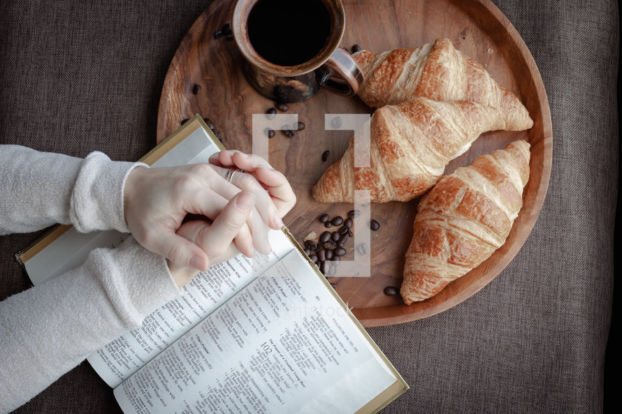 praying hands over a Bible and coffee and croissants 