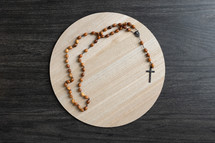 Wood rosary on a light wood round tray on a dark wood background