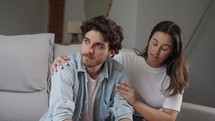 Young caucasian man sit with wife indoor feels upset, loving woman put hand on shoulders hugs him comforting, express empathy, close up. Crisis, impotence, potency health problems, incurable disease concept
