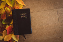 Closed black bible on a wood background with an autumn leaf border