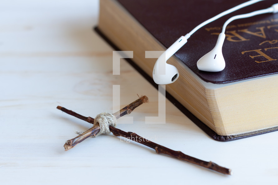 earbuds on a Bible and cross made of sticks 