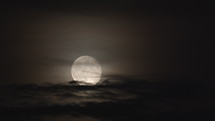 Slowly rising full moon in a night sky