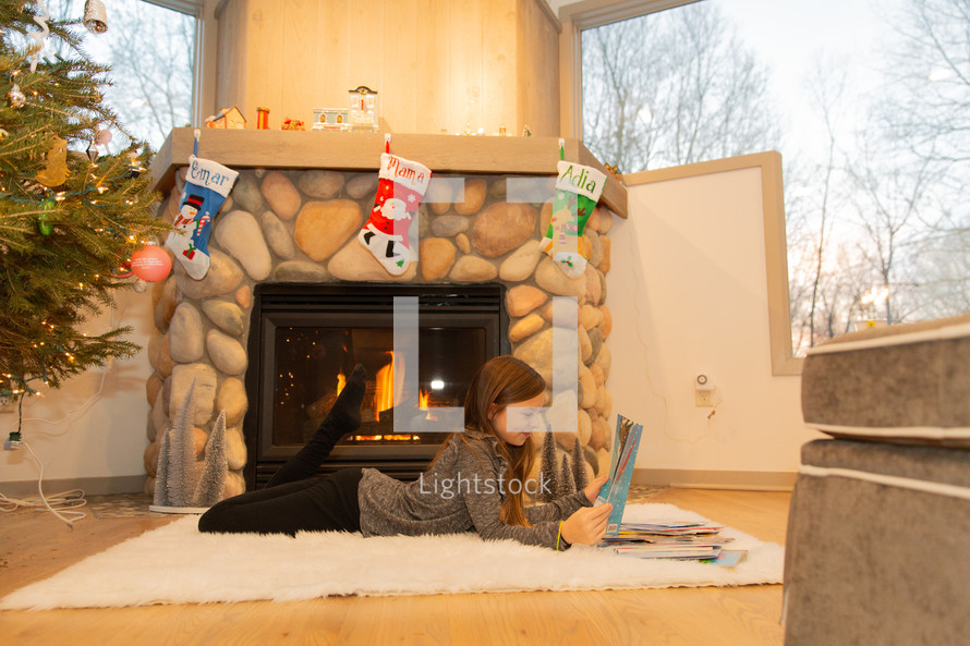 girl reading a Christmas book by a fireplace 