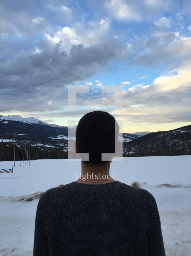 man standing with his back to the camera facing snow 